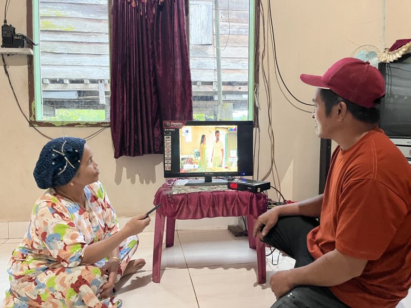 Ibu Mude (kiri), Masyarakat Desa Olu, kini dapat menikmati listrik dengan nyaman untuk aktivitas sehari-hari, termasuk menonton televisi tanpa lagi bergantung pada accu. Kehadiran listrik PLN membawa perubahan nyata bagi kualitas hidup masyarakat, membuka akses informasi melalui konektivitas digital saluran TV dan membuka peluang baru bagi peningkatan ekonomi masyarakat di wilayah terpencil.
