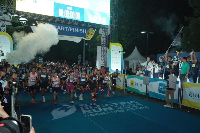 Direktur Utama PLN, Darmawan Prasodjo (belakang memegang bendera) bersama jajaran Direksi dan Komisaris PLN melepas para peserta Kategori Half Marathon PLN Electric Run 2025 di garis start.