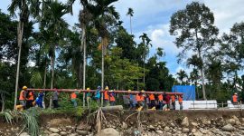 Sejumlah petugas PLN bahu-membahu memikul tiang jaringan listrik secara manual untuk menembus wilayah yang terisolir akibat bencana. Meskipun terdapat 171 titik longsor yang memutus akses jalan darat, PLN terus berupaya mempercepat pemulihan infrastruktur kelistrikan di 68 desa tersisa.